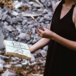 A woman performs a mystical ritual outdoors, holding a candle and spell book.