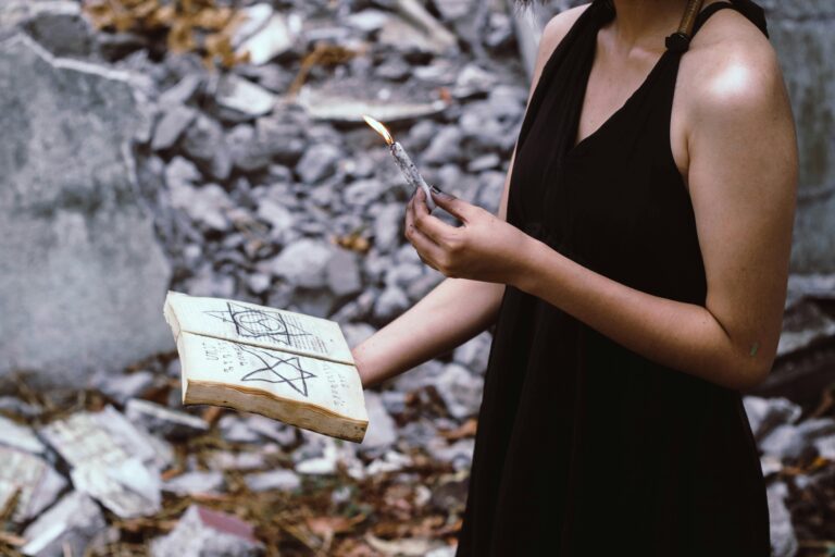 A woman performs a mystical ritual outdoors, holding a candle and spell book.