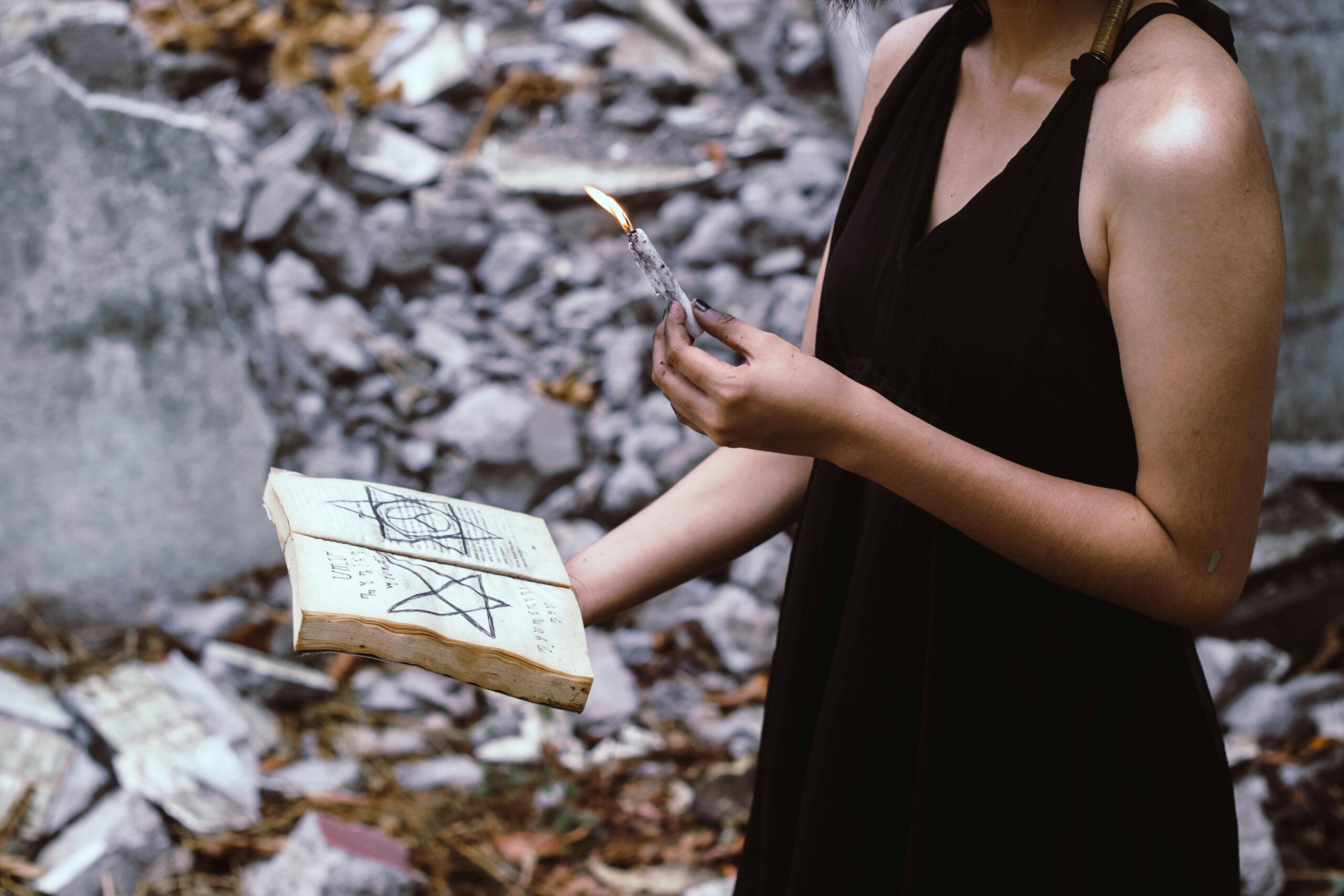 A woman performs a mystical ritual outdoors, holding a candle and spell book.