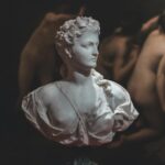 A marble bust sculpture displayed in a dimly lit, classic art gallery.